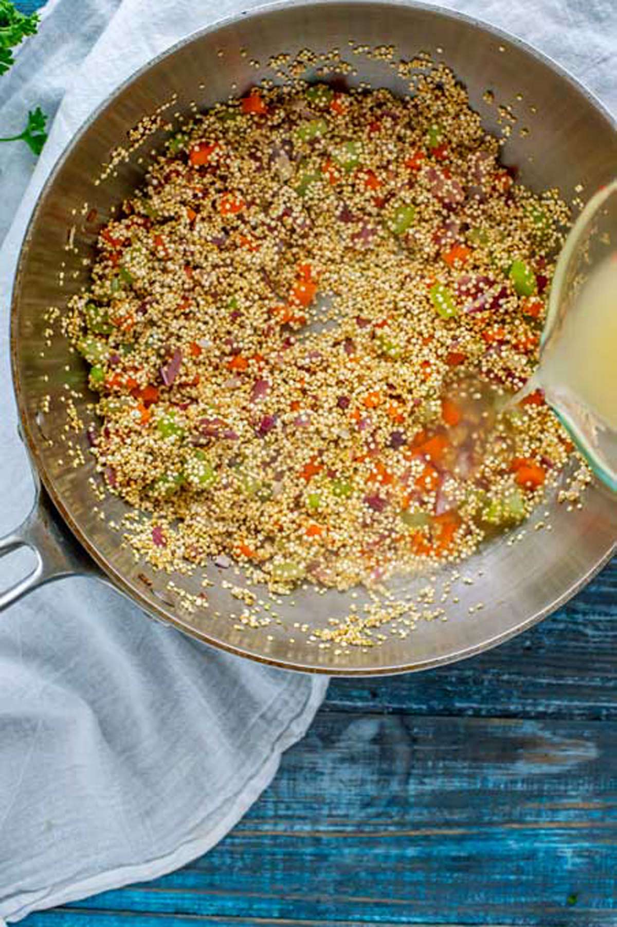 Quinoa in a pot with broth being poured into it.