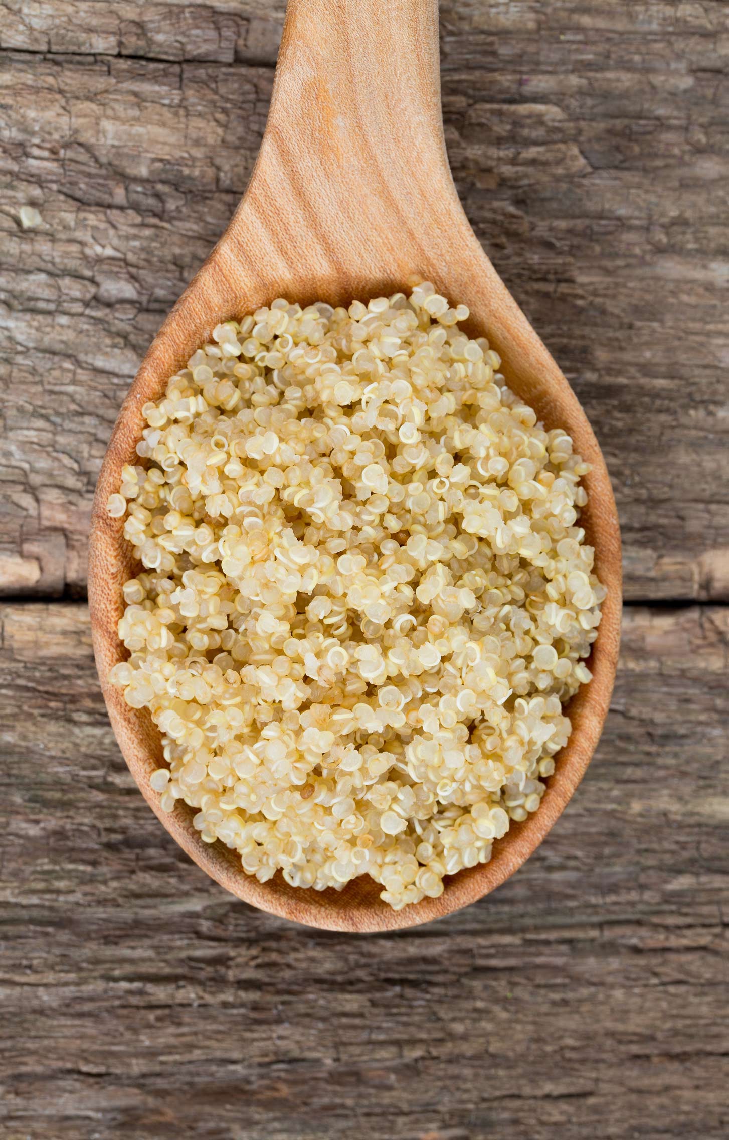 A wooden spoon with cooked quinoa on a rustic wooden background.