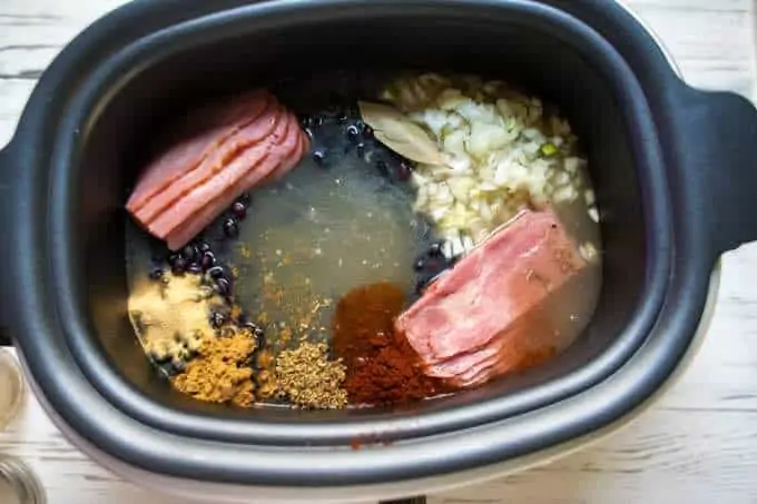 Photo of broth being added to a slow cooker that is already filled with all of the ingredients for Slow Cooker Black Beans