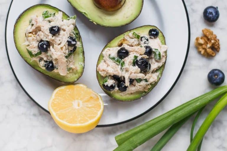 Aerial view of a plate with blueberry chicken salad stuffed avocados with lemon wedge, green onions and blueberries. 