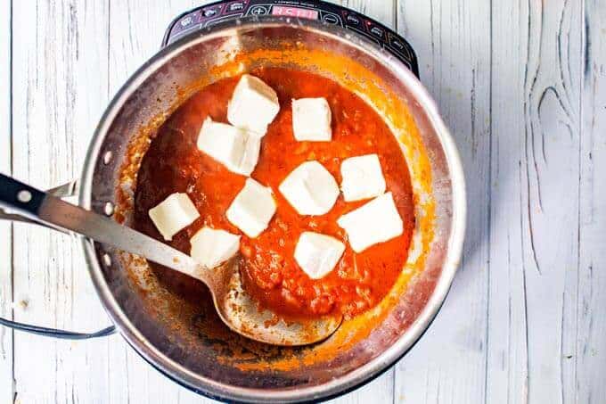 Photo of cubes of cream cheese being added to a pot with tomato sauce.