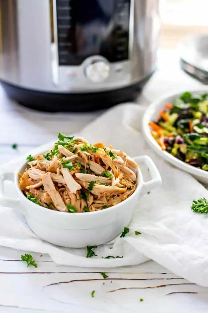 Photo of Instant Pot Shredded Chicken in a white dish and garnished with parsley taken from the side.