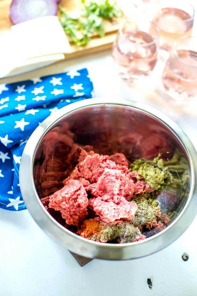 Photo of ground beef, pesto and seasonings in a bowl for Italian Burgers.
