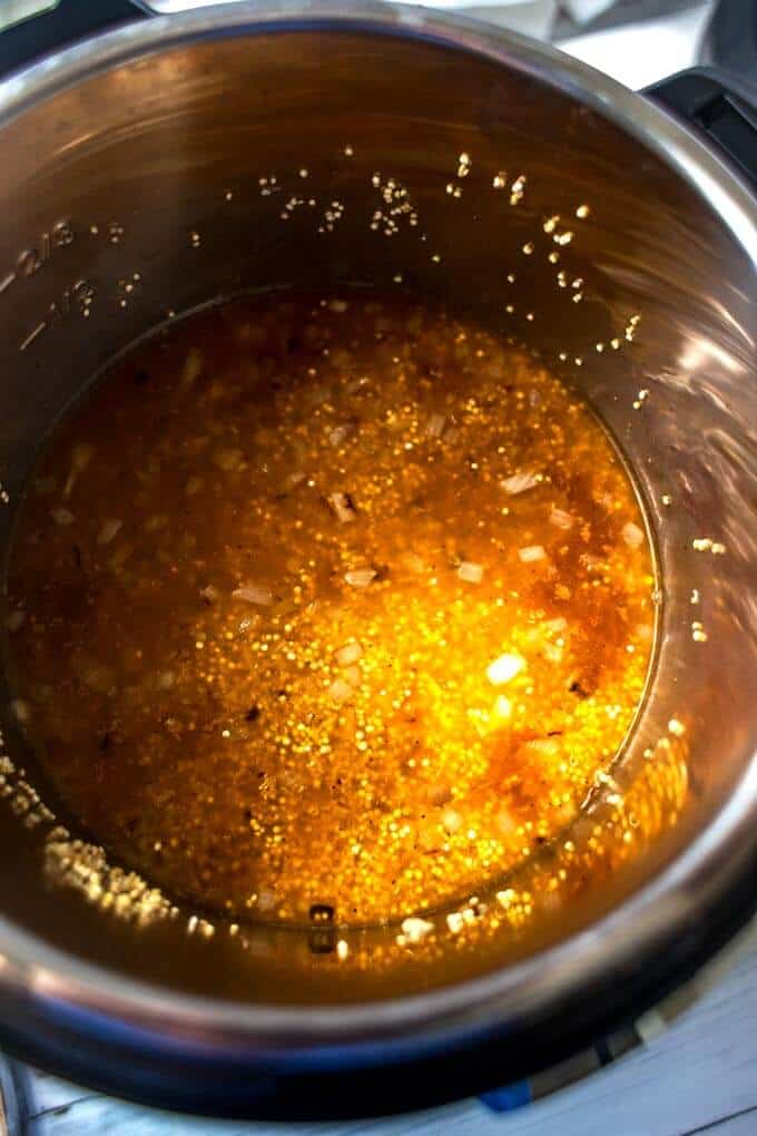 Photo of vegetable broth being added to toasted quinoa, onion, and garlic in an Instant Pot.