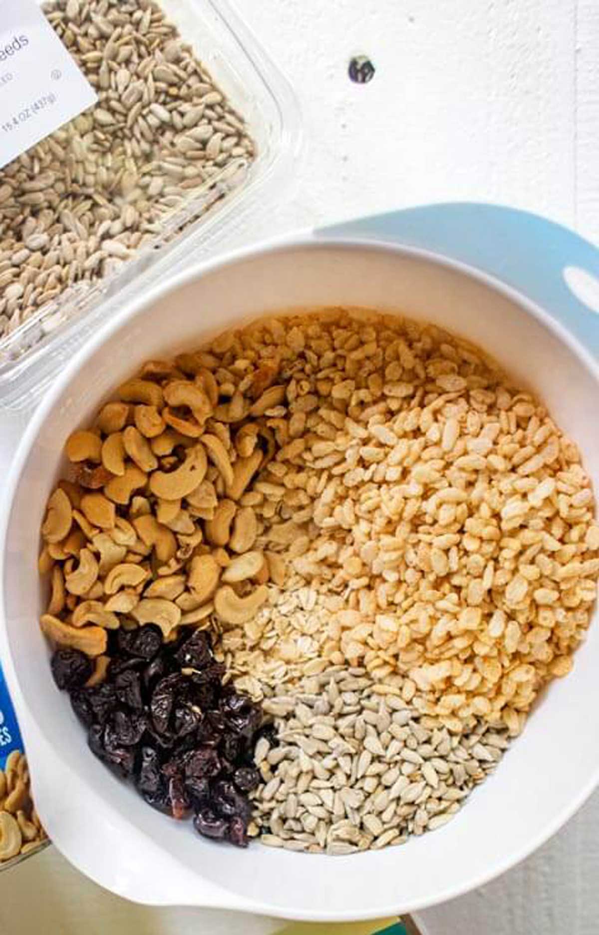 Photo of dry ingredients for a homemade granola bar recipe mixed together in a bowl with the ingredient packaging surrounding.