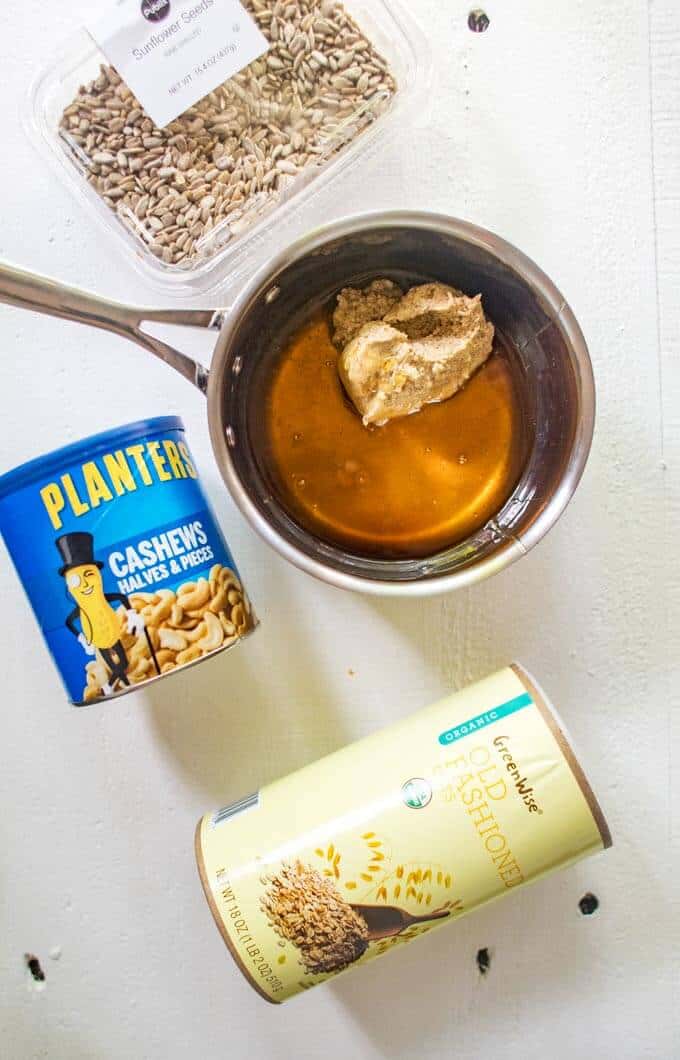 Photo of wet ingredients for a homemade granola bar recipe mixed together in a saucepan with the dry ingredients in packages surrounding.