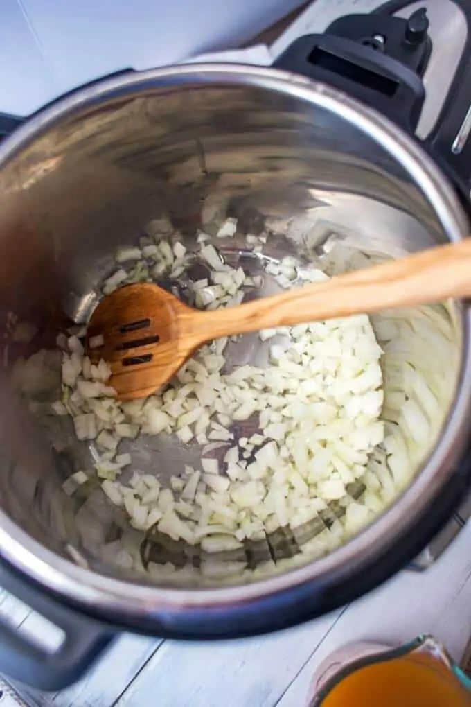 Photo of an Instant Pot with onion cooking in it and a wooden spoon.