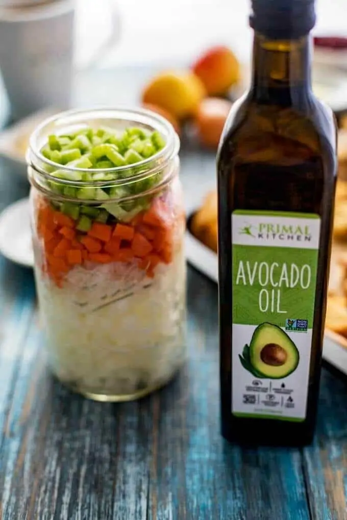 Photo of a mason jar with chopped onion, carrot, and celery and a bottle of avocado oil.