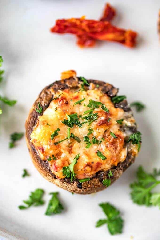 Close up photo of a vegetarian stuffed mushroom on a white plate garnished with parsley.