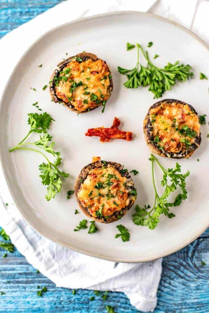 Round white plate of three vegetarian stuffed mushrooms garnished with parsley and sun dried tomatoes.