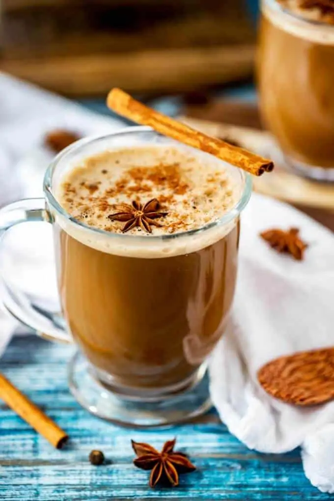 Photo of a Dirty Chai Latte in a glass mug garnished with ground cinnamon, a cinnamon stick, and a star anise.