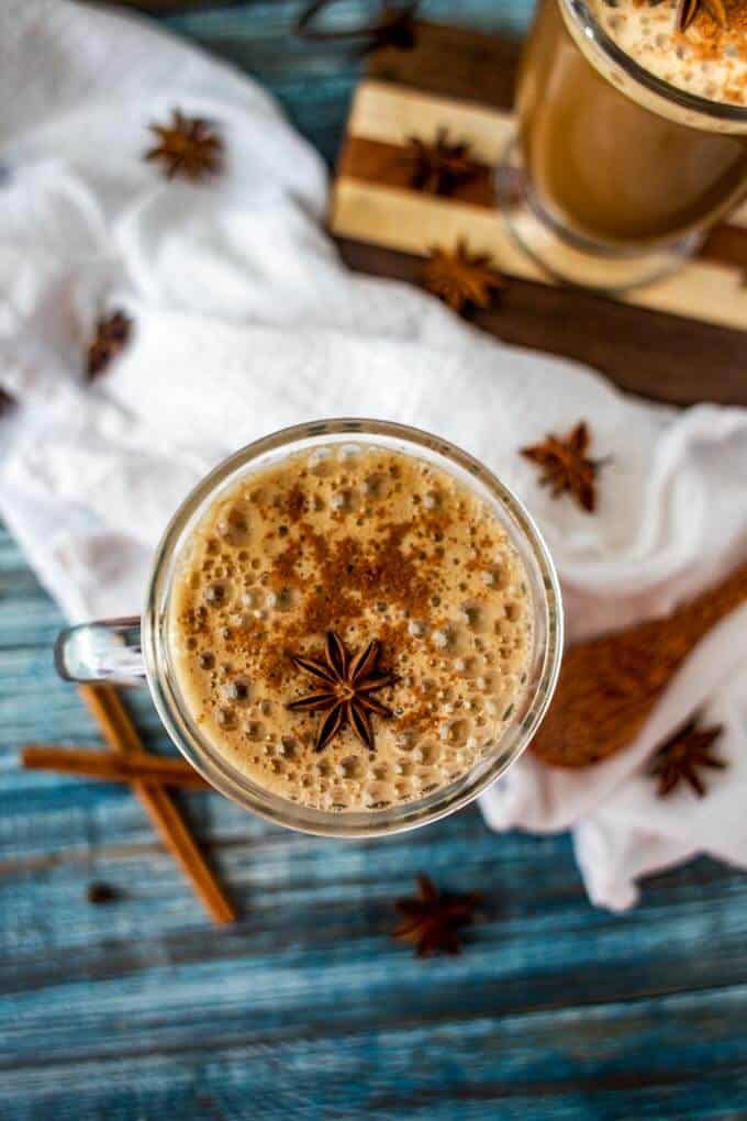 Overhead photo of a Dirty Chai Latte in a glass mug with star anise and cinnamon sticks scattered.
