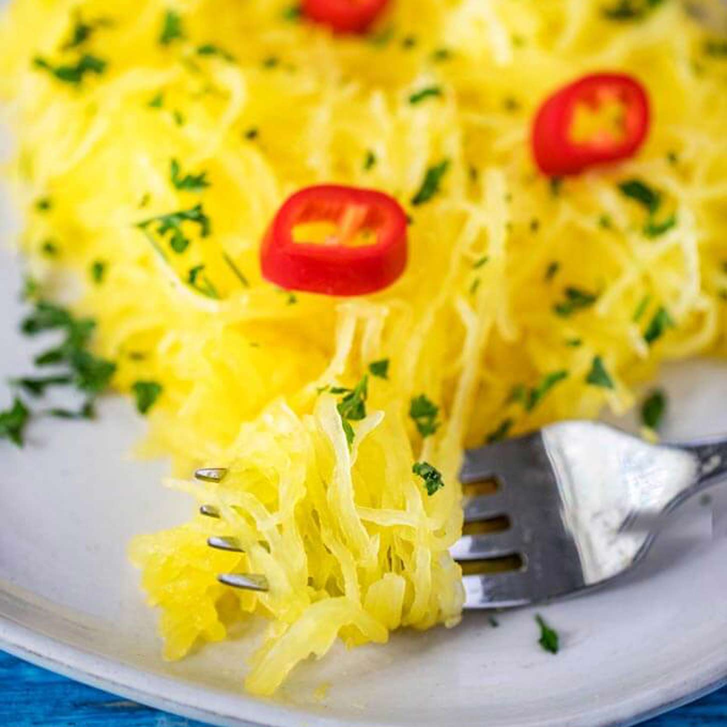 Close up square photo of Instant Pot Spaghetti Squash on a fork, garnished with hot peppers and parsley.