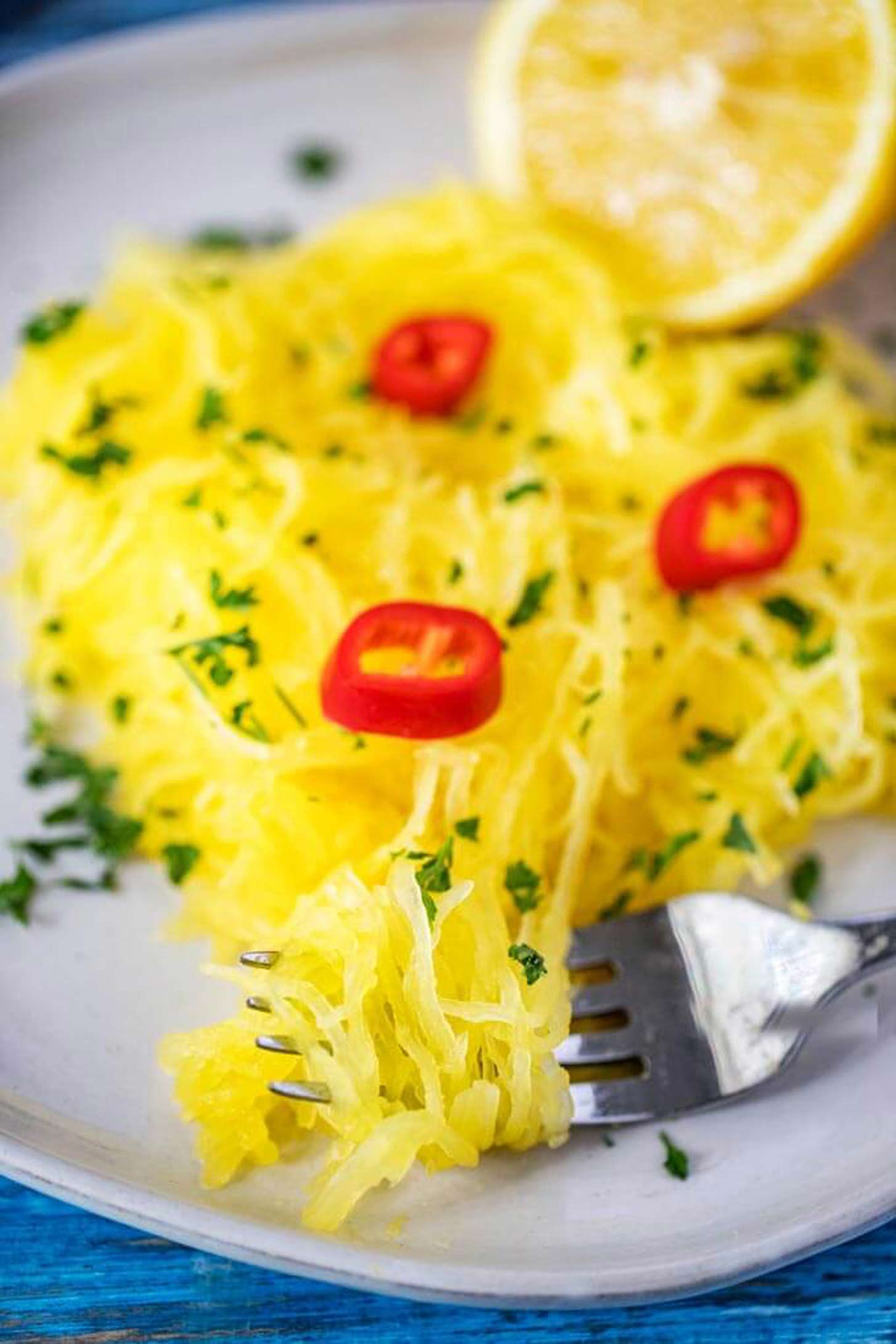 Close up photo of Instant Pot Spaghetti Squash on a fork, garnished with hot peppers and parsley with a lemon.