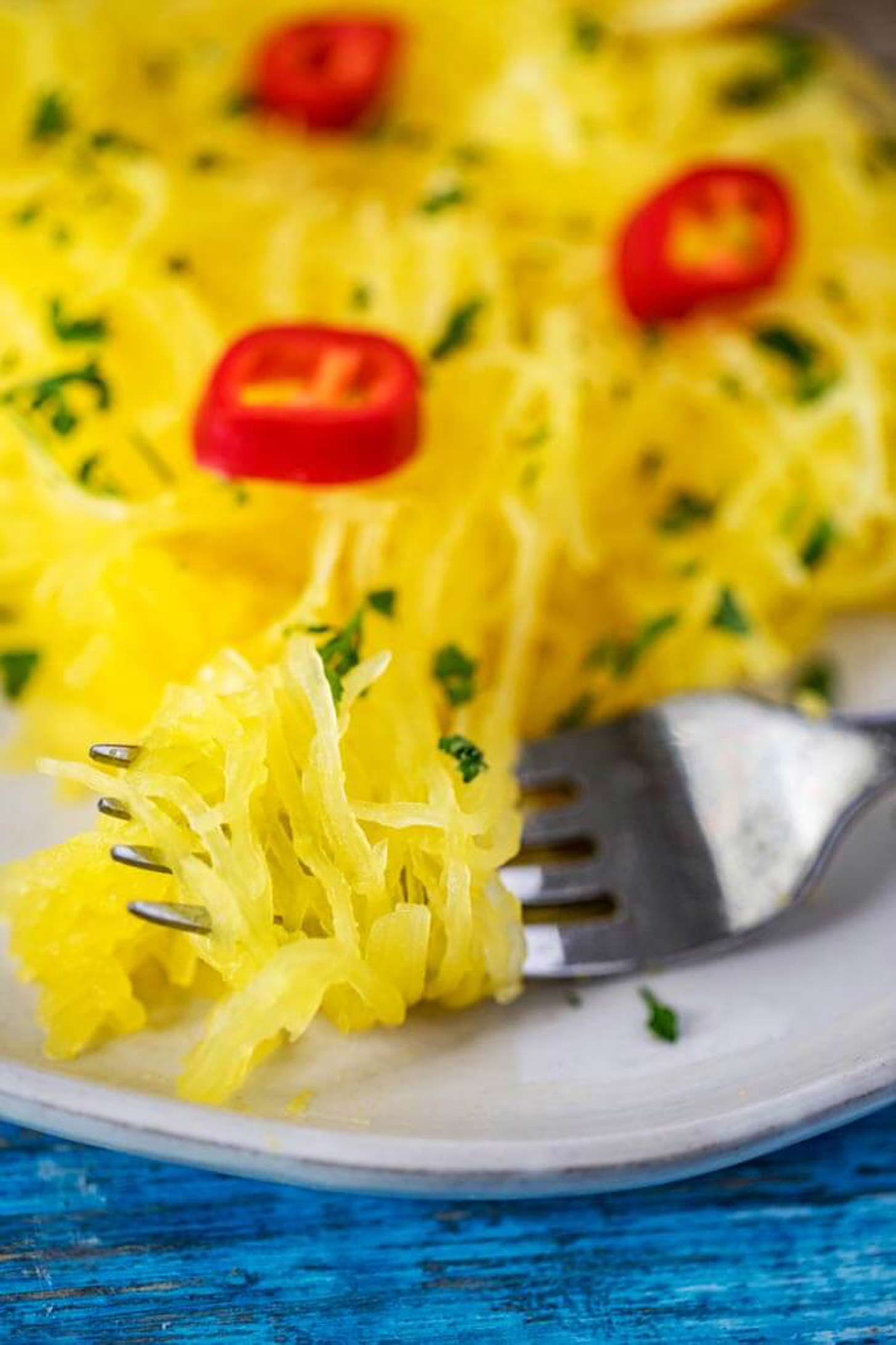 Close up photo of Instant Pot Spaghetti Squash on a fork garnished with parsley and hot peppers.