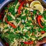 Photo of Vegetarian Paella in a skillet with a spoon garnished with lemon and parsley.