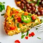 Close up photo of a zucchini frittata on a white plate garnished with jalapeno, tomato, and cilantro.