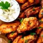 Close up photo of Air Fryer Chicken Wings on a parchment lined plate garnished with parsley and a small dish with blue cheese sauce in it.