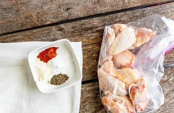 Seasoning mixture in a small white prep bowl sitting next to a zip top bag of chicken wings.