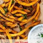 Photo of air fryer sweet potato fries on parchment paper garnished with parsley.
