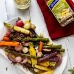 Overhead photo of Roasted Spring Vegetables on a white platter sitting on a wooden white background with thyme next to it and a bottle of Holland House White Cooking Wine.