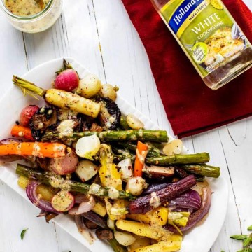 Overhead photo of Roasted Spring Vegetables on a white platter drizzled with a mustard wine dressing. There is a bottle of Holland House White Cooking Wine sitting on a red napkin next to it.