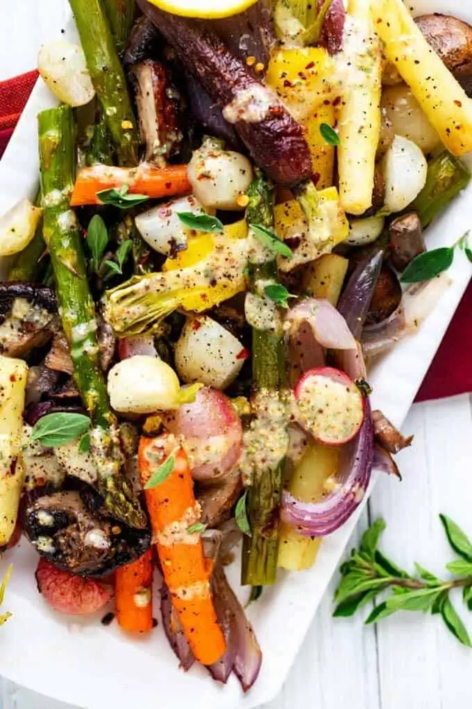 Close up photo of Roasted Spring Vegetables on a white platter garnished with thyme and drizzled with a mustard vinaigrette.