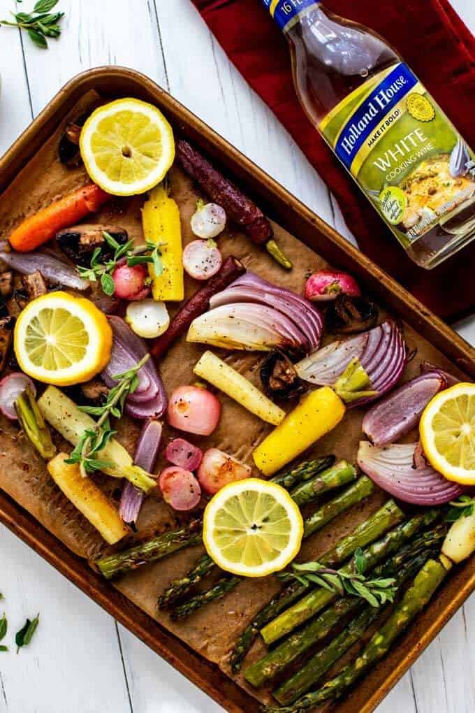 Roasted Spring Vegetables on a sheetpan garnished with lemon and thyme sprigs with a bottle of Holland House White Cooking Wine sitting next to it.