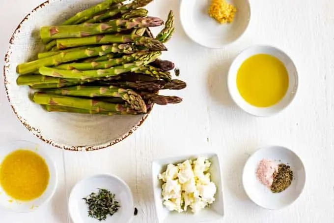 Photo of asparagus, garlic, oil, lemon juice, seasonings, goat cheese, and thyme in small white prep bowls.