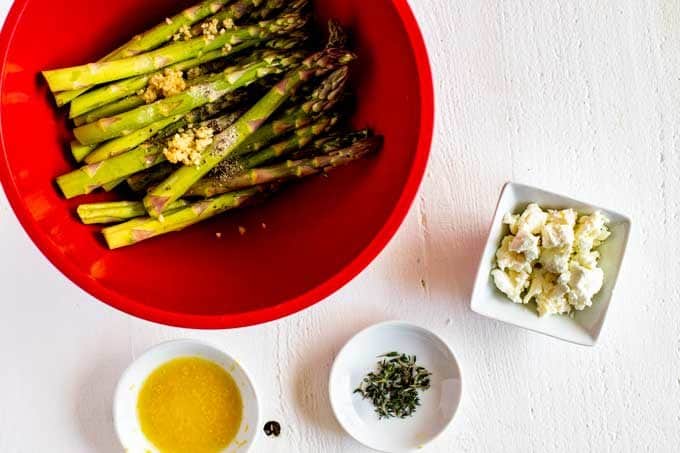 Photo of seasoned asparagus in a bowl with toppings surrounding in in small bowls.