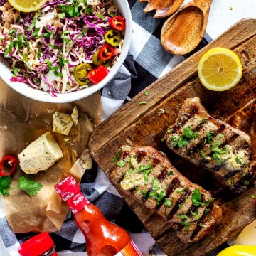 Overhead photo of a prepared grilled steak recipe with butter on top sitting on a cutting board with a bowl of spicy slaw next to it.