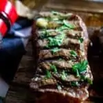 Close up photo of a grilled steak on a wooden cutting board garnished with parsley.
