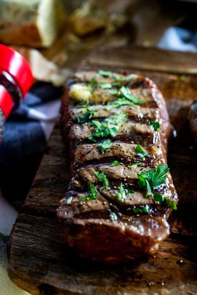 Close up photo of a grilled steak on a wooden cutting board garnished with parsley.