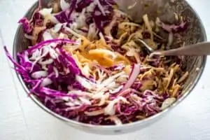 Photo of slaw dressing being poured over slaw in a metal bowl.