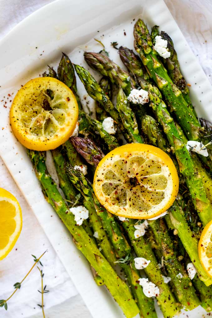 ¾ overhead photo of Air Fryer Asparagus on a white platter garnished with lemons.