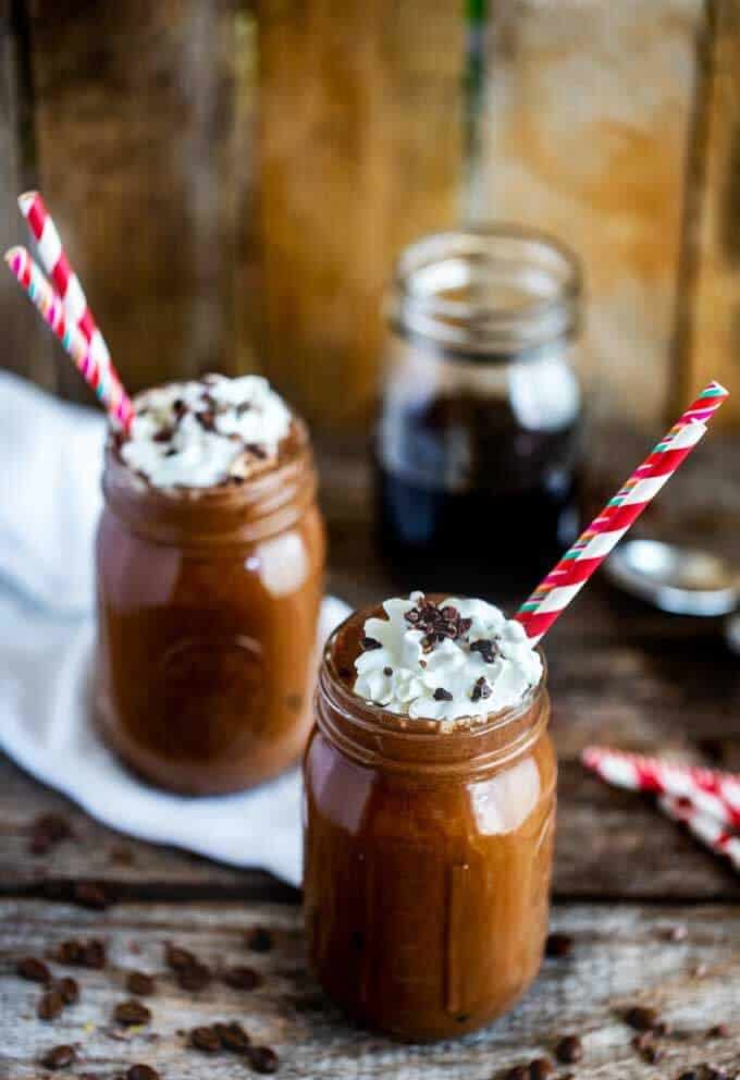 Photo of two mason jars on a dark background with Iced Mocha Lattes in them and coffee beans scatterd around.