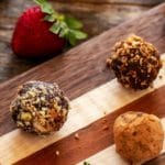 Photo of three gluten free truffles on a wooden cutting board with a strawberry next to it.