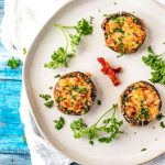 Square photo of three stuffed mushrooms on an off-white plate.