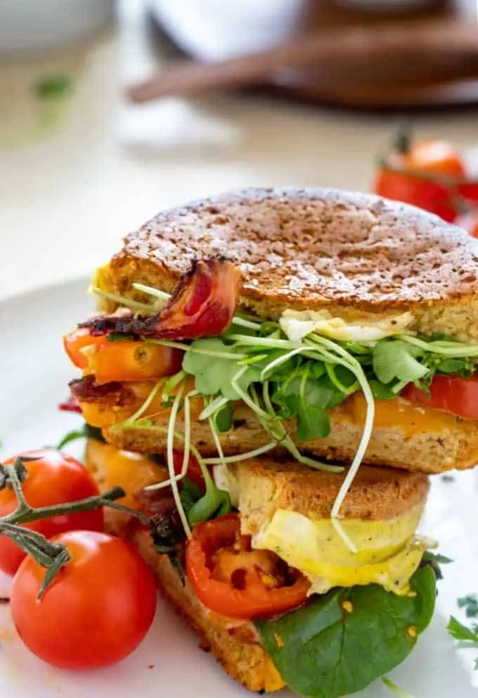 Side photo of a gluten free breakfast sanwich on a white plate with cherry tomatoes by it.