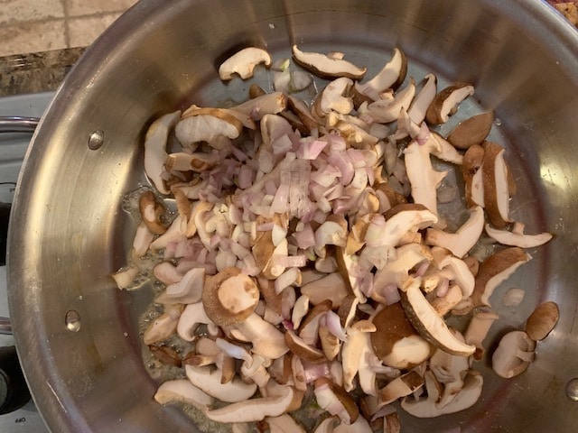 Photo of mushrooms and shallots in a large skillet.