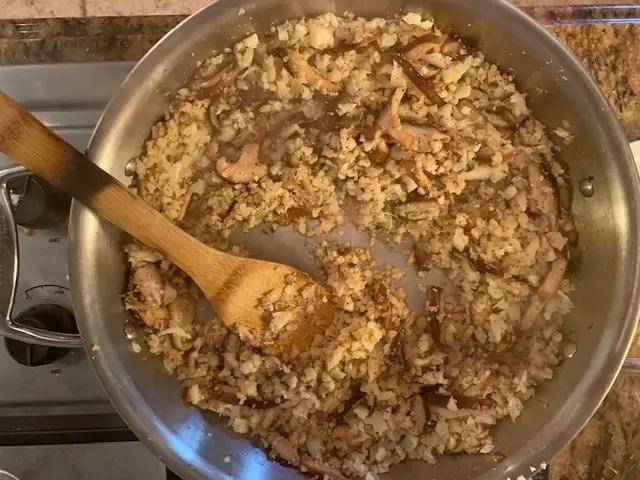 Photo of cauliflower rice and mushrooms in a large skillet that has had cooking wine added to it and been cooked.