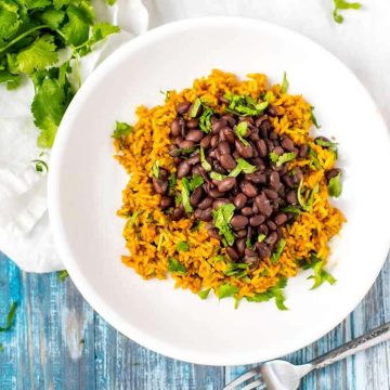 Overhead photo of Slow Cooker Black Beans over yellow rice on a white plate.