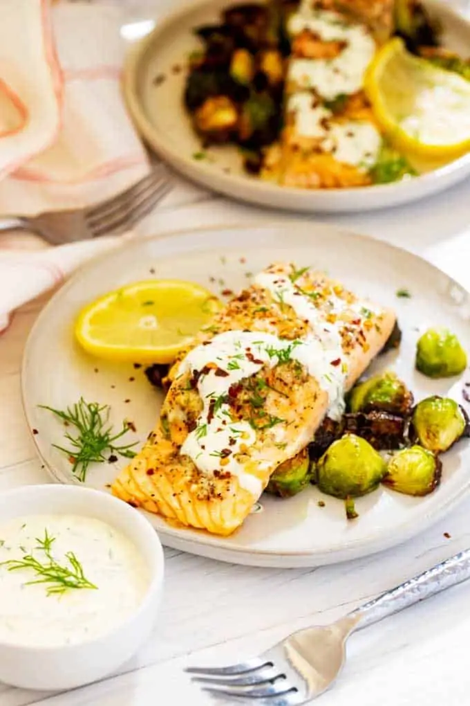 Photo of two plates of Garlic Salmon with a bowl of lemon dill sauce next to the front one.