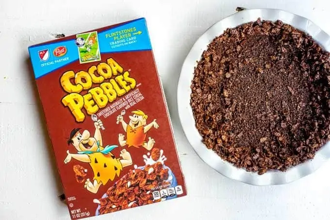 Photo of a pie plate with a chocolate cereal pie crust and a box of cocoa pebbles next to it.