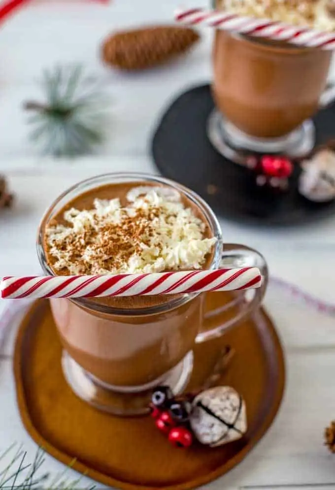 Photo of two glasses of Crock Pot Hot Chocolate with whipped cream and a mint stick on top.