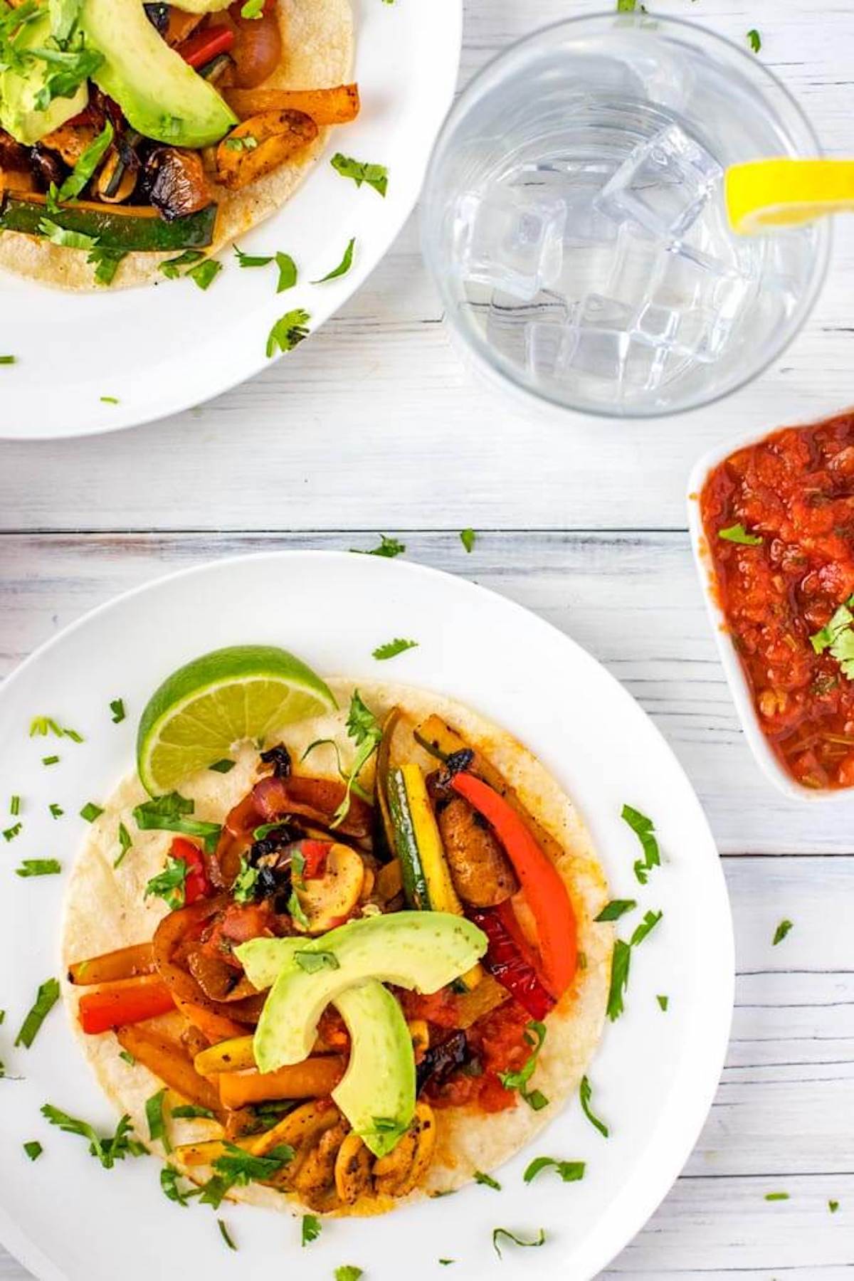 Overhead photo of vegetarian fajitas on white plates garnished with cilantro.