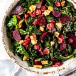 Close up overhead photo of a kale beet salad in a rustic white bowl.