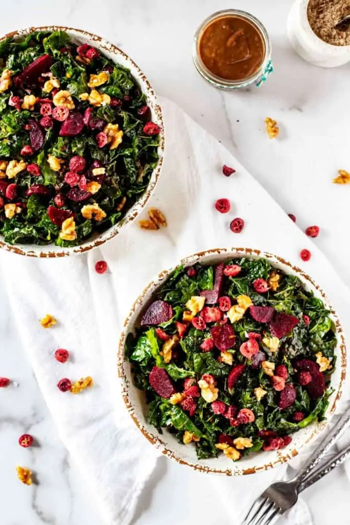 Overhead photo of two rustic bowls with Kale Beet Salad on a white background.
