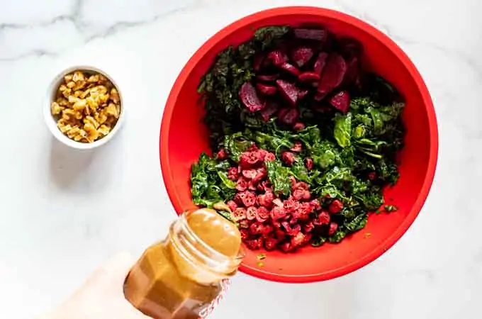 Photo of a bowl with kale, beets, and cranberries with balsamic vinaigrette being poured over it.