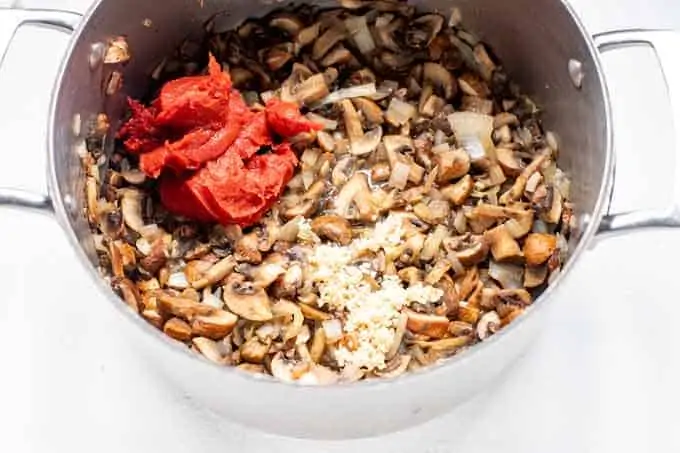Photo of large pot with mushrooms, onions, tomato paste, and garlic in it.